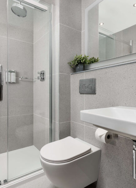 Modern bathroom with white fixtures: sink, toilet, and bathtub. Elegant dark wood accents, hanging plants, large mirror, and natural light create a clean and relaxing atmosphere.