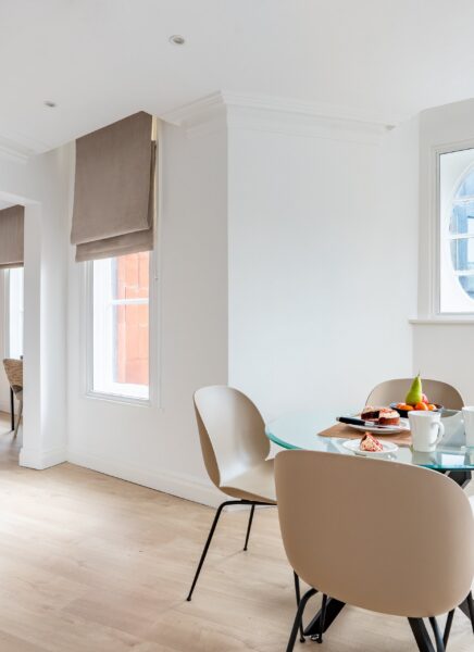 A modern hotel suite with a plush double bed, stylish furniture, city skyline view through large windows, and ambient lighting, creating a cozy and luxurious atmosphere.