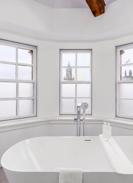 A modern apartment building with large windows, surrounded by trees and streetlights, under a cloudy sky.