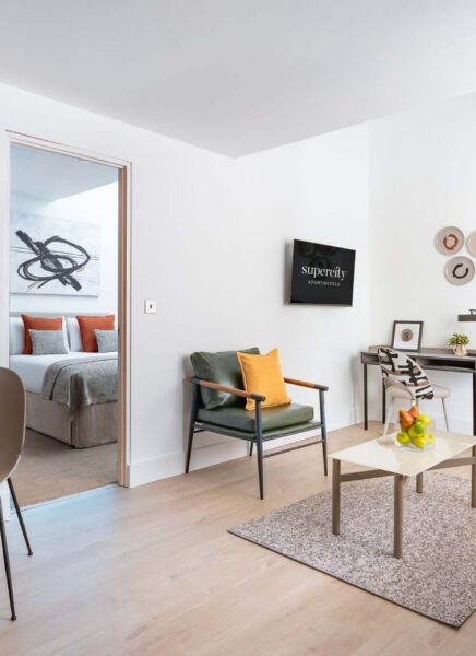 Image shows a modern, stylish one-bedroom suite with a large bed, sleek furniture, and contemporary decor. A spacious living area and floor-to-ceiling window offer city views.