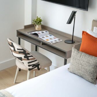 The image shows a modern hotel lobby featuring sleek furniture, a reception desk, decorative plants, and large windows allowing natural light. The atmosphere is contemporary and inviting.