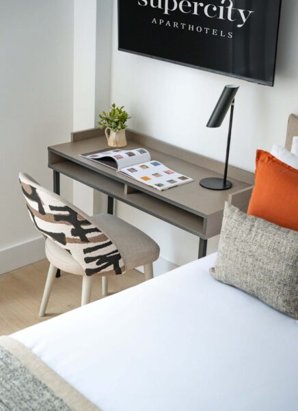 The image shows a modern hotel lobby featuring sleek furniture, a reception desk, decorative plants, and large windows allowing natural light. The atmosphere is contemporary and inviting.