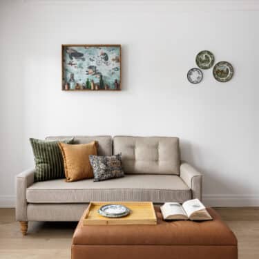 A cozy, modern living room featuring a plush green sofa, round wooden coffee table, large windows with city views, and decorative plants for a refreshing atmosphere.
