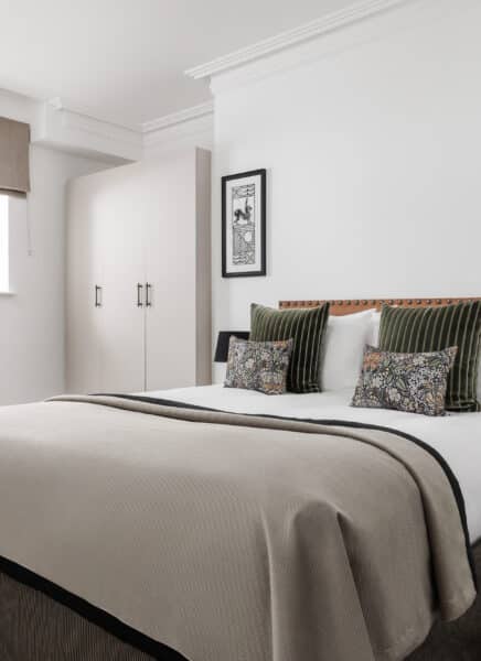 A modern kitchen with sleek white cabinets, marble countertops, stainless steel appliances, pendant lights, and a wooden dining table with chairs, set in a stylish, well-lit room.