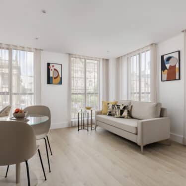 Chic and modern living area with a grey sofa, large windows, a coffee table, and a stylish lamp, complemented by neutral tones and minimalist decor.