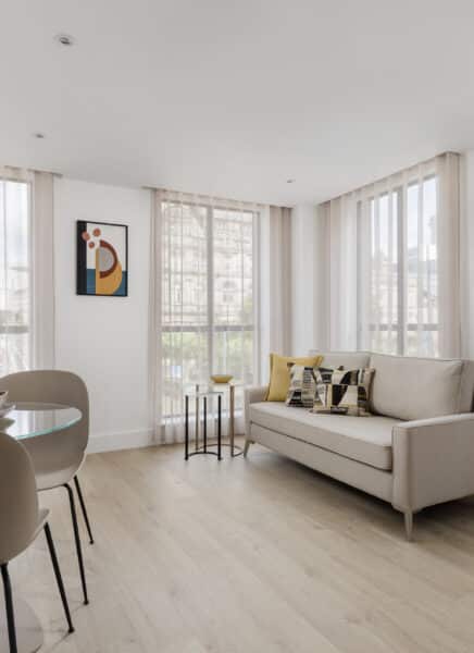 Chic and modern living area with a grey sofa, large windows, a coffee table, and a stylish lamp, complemented by neutral tones and minimalist decor.