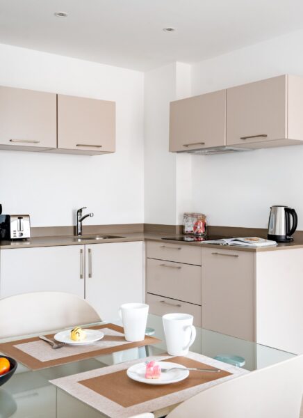 A well-lit, modern kitchen with wooden flooring, featuring a large center island, bar stools, sleek cabinetry, stainless steel appliances, and a spacious dining area with contemporary décor.