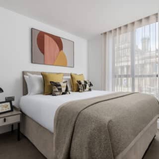 A modern hotel room with a large bed, wooden flooring, seating area, and a flat-screen TV mounted on the wall.
