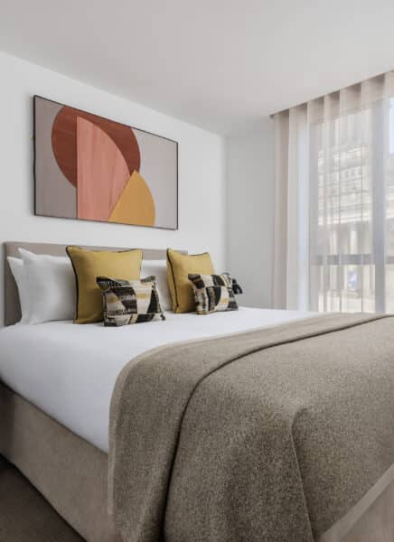 A modern hotel room with a large bed, wooden flooring, seating area, and a flat-screen TV mounted on the wall.