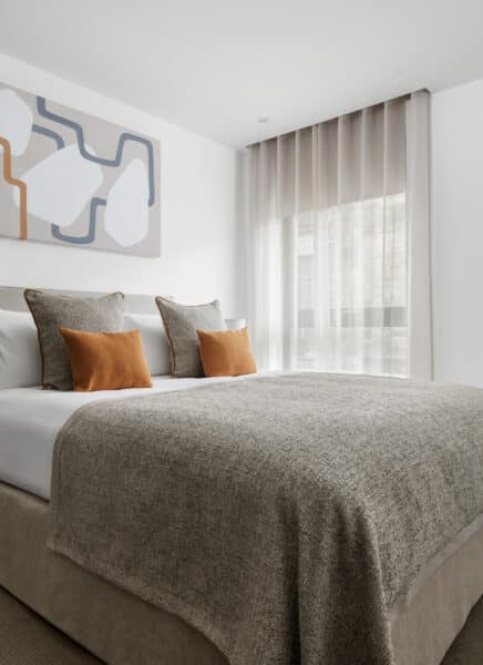 A modern, fully furnished bedroom with a large, comfortable bed, well-lit interiors, two bedside tables with lamps, and a scenic window view, creating a cozy, inviting atmosphere.