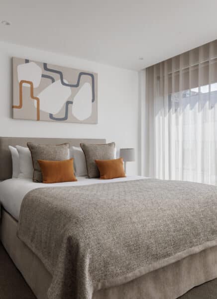 A modern, well-lit hotel room with a large bed, artistic wall decor, a desk, and a window offering a city view.