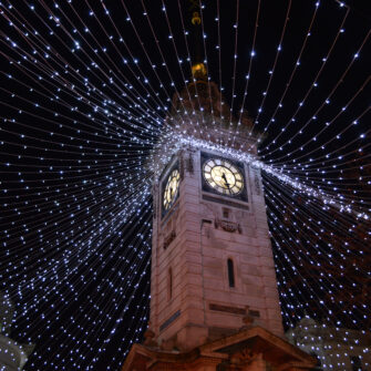 A modern kitchen with white cabinetry, a marble countertop, wooden bar stools, and stainless steel appliances, featuring pendant lights and decorative items for a stylish and functional space.