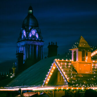 A modern, stylish studio apartment with a cozy bed, kitchen area, and a small dining table. Large windows allow natural light, with neutral-tone decor creating a warm atmosphere.