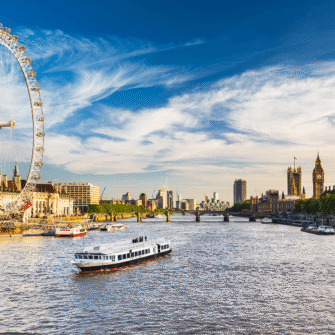 Aerial view of London, showcasing iconic landmarks like the River Thames, London Eye, and Shard under a clear blue sky.