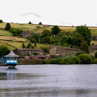 A scenic view of the rolling hills and lush landscape of Haworth and Brontë Country, featuring vibrant green fields and a cloudy sky.