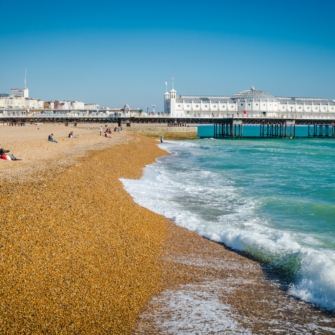 A scenic view of Brighton Beach with a row of colorful beach huts and the sea in the background under a partly cloudy sky.
