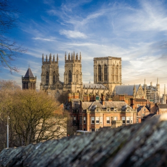 Image depicts the stunning cityscape of York, featuring historic buildings, a clear blue sky, and the iconic York Minster standing prominently in the background.